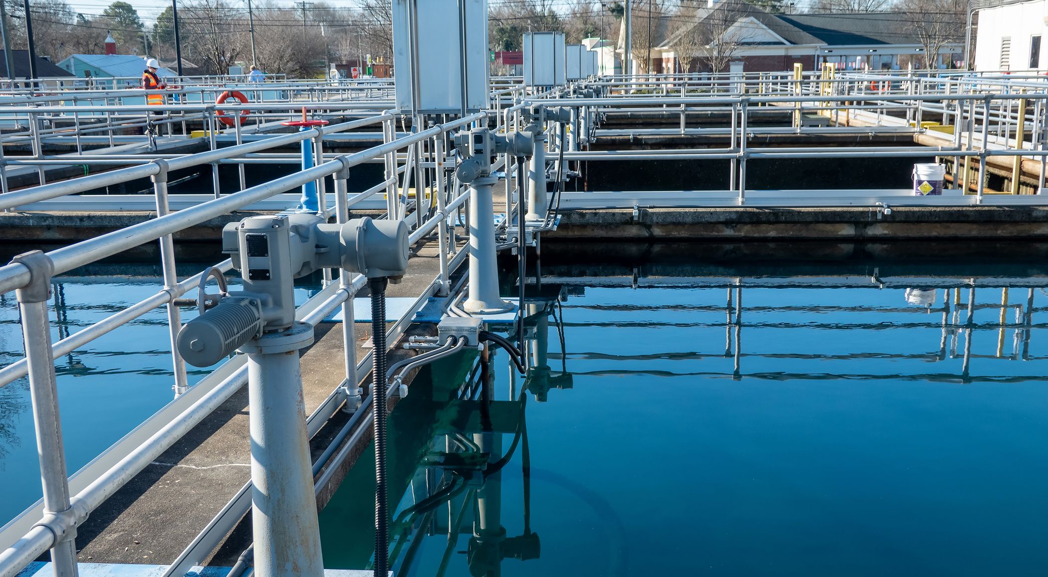 Enisca Browne - Water treatment facility with metal railings and large concrete tanks filled with clear blue water.