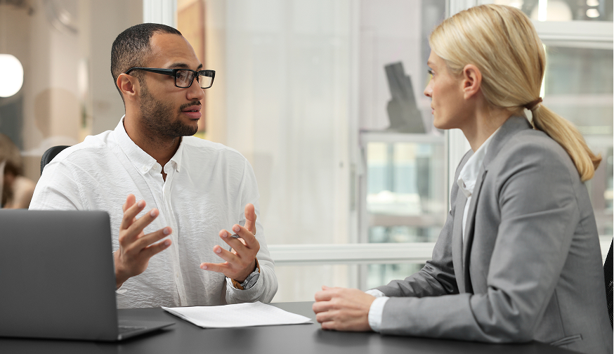 Enisca Browne - A man and woman in business attire have a serious discussion at a desk in a modern office.