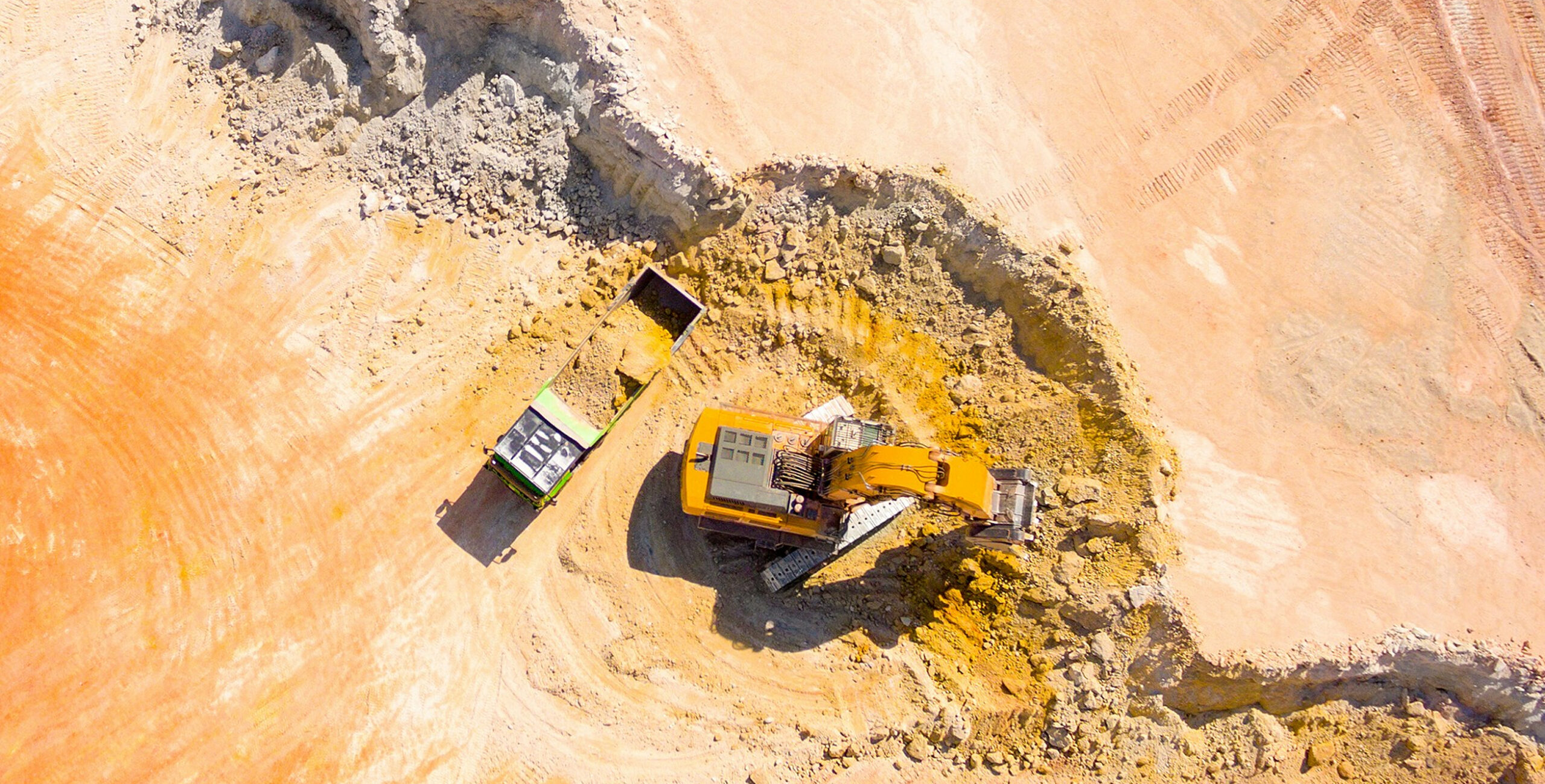 Enisca Browne - Aerial view of an excavator loading dirt into a dump truck at a construction site.