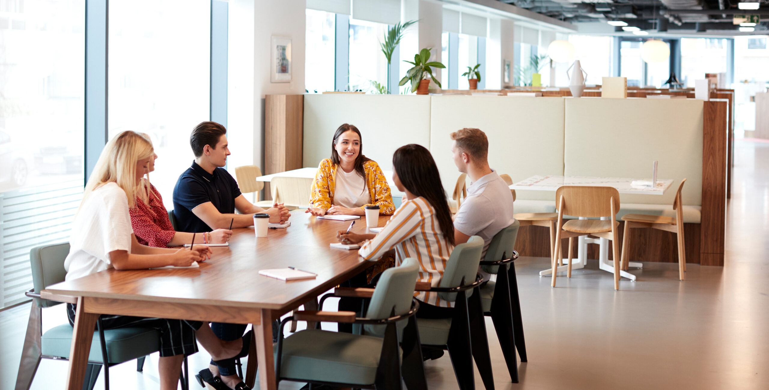 Enisca Browne - Six people sit around a table in a modern office, engaged in a meeting and conversation.