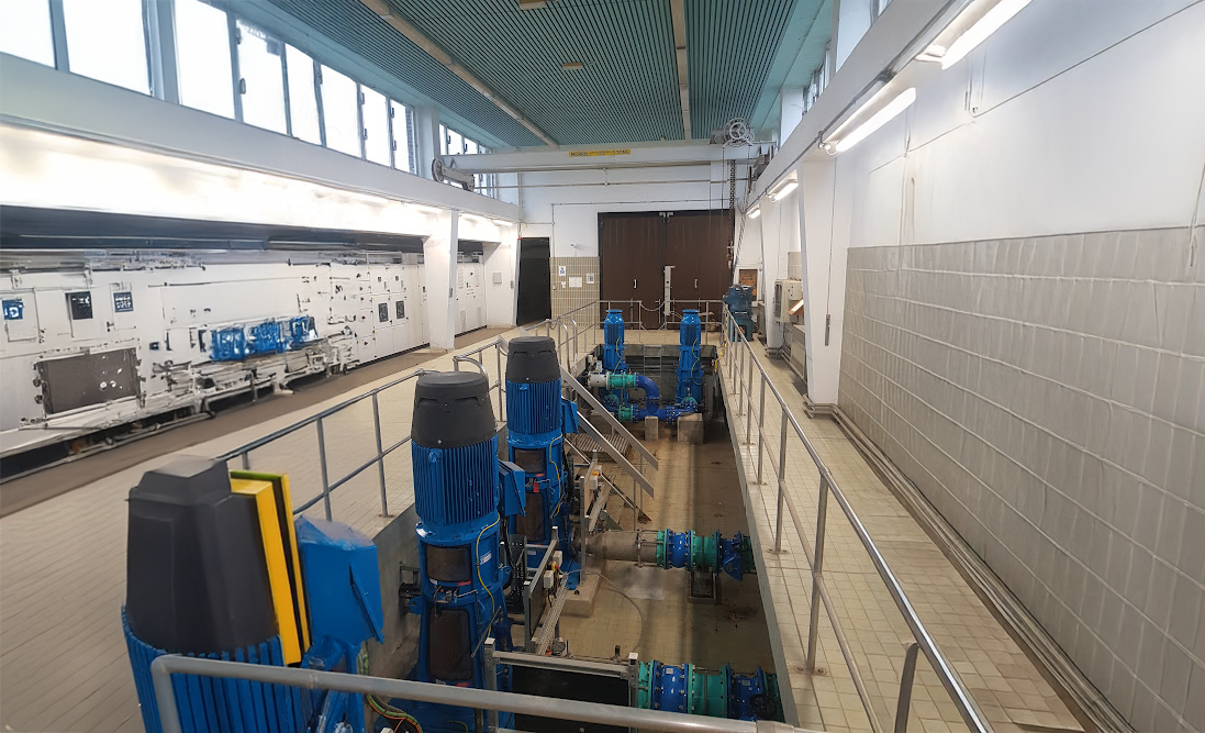 Enisca Browne - A row of blue industrial pumps and pipes inside a clean, well-lit facility with tiled walls and floors.