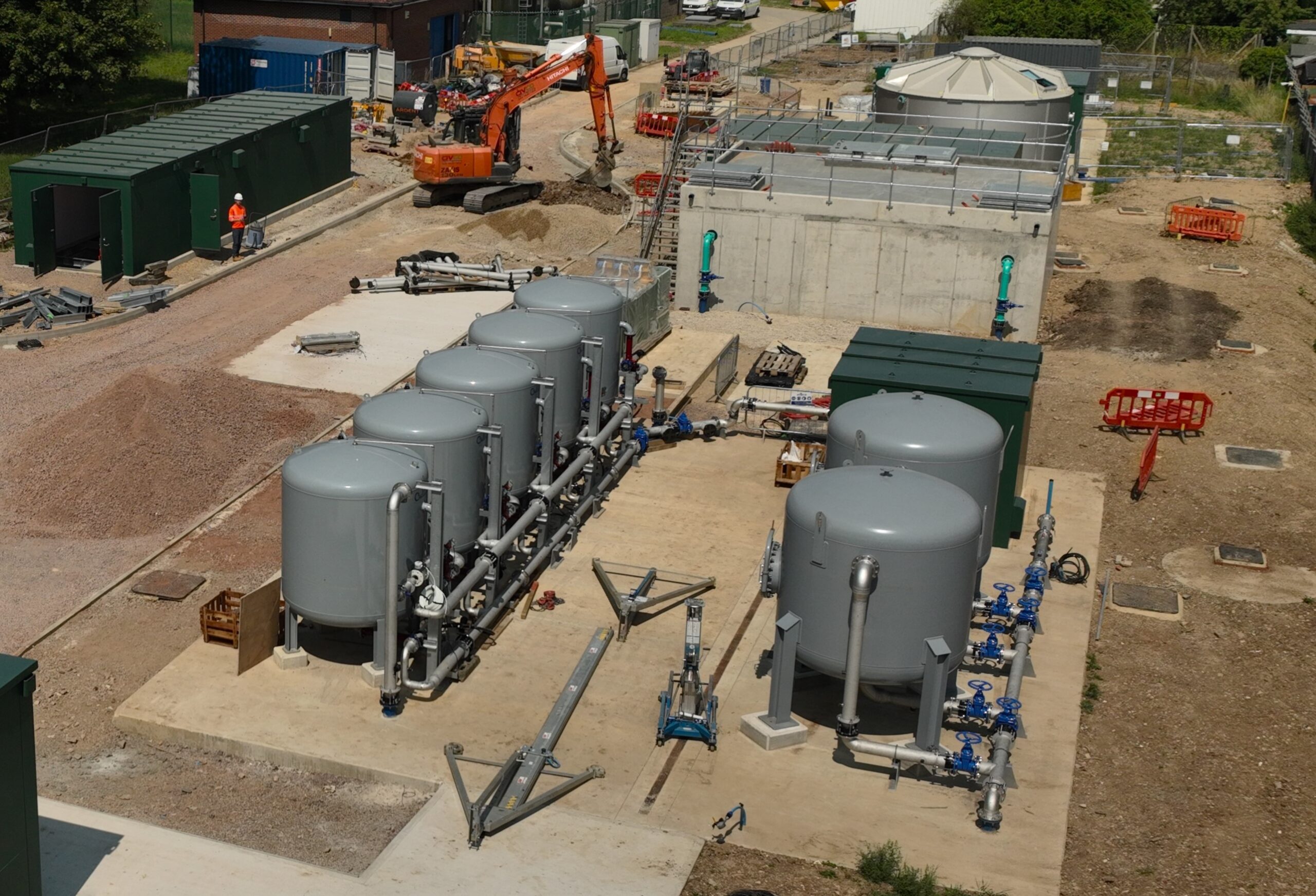 Enisca Browne - Aerial view of an industrial facility with large storage tanks, pipes, and construction equipment.