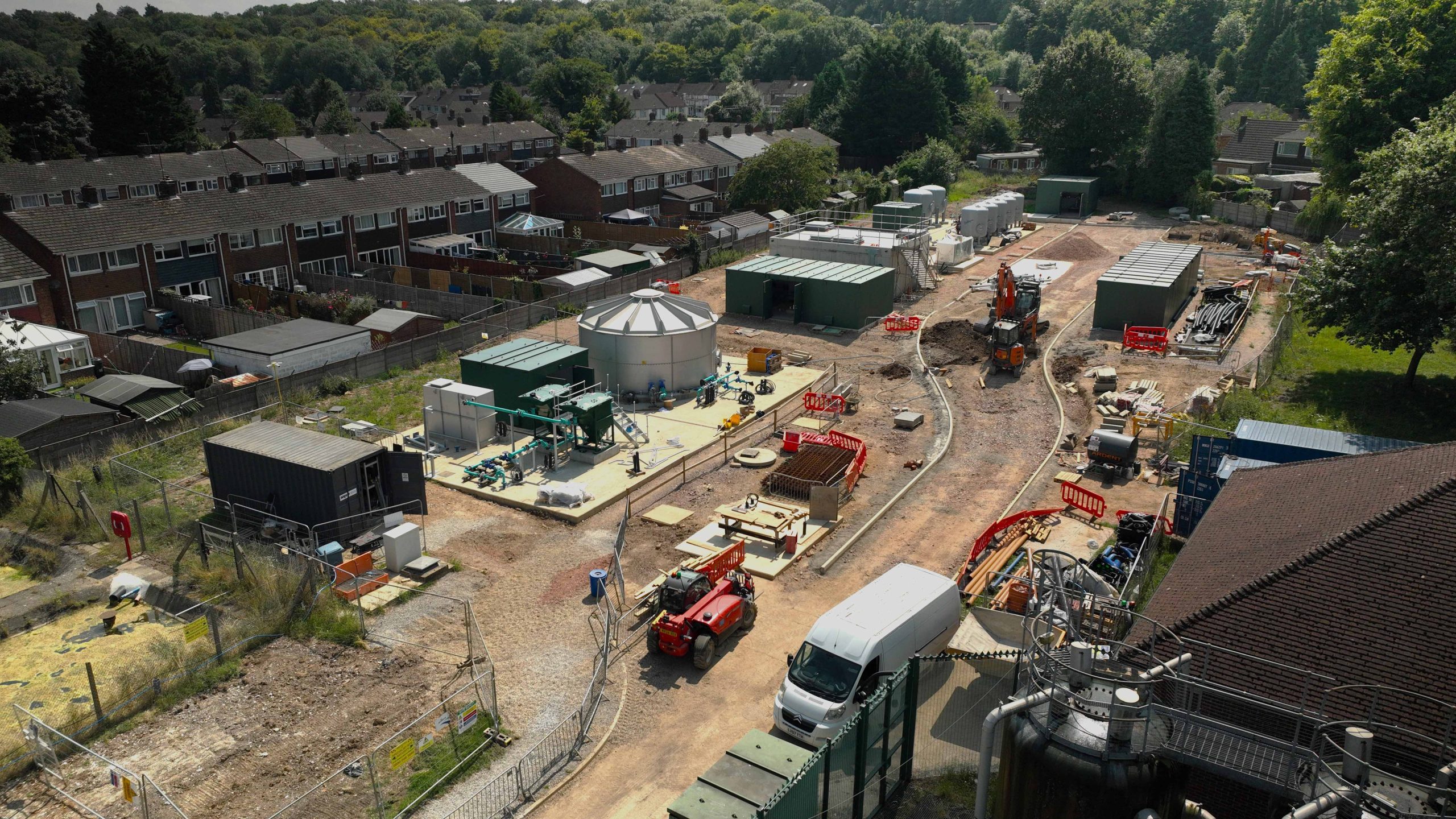 Enisca Browne - Aerial view of a construction site near residential houses with various vehicles and equipment.
