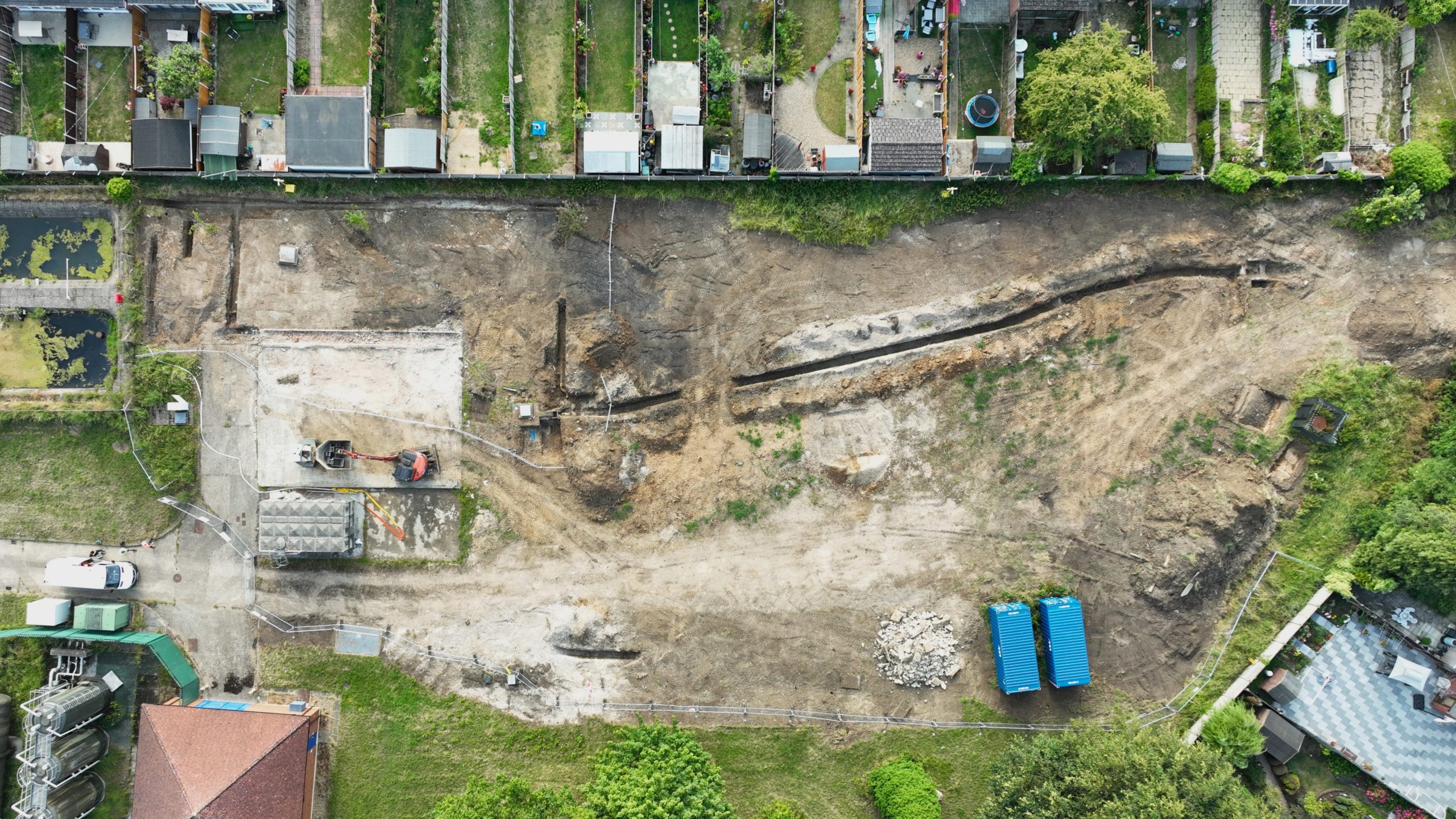 Enisca Browne - Aerial view of a construction site with machinery, dirt paths, and blue materials near residential buildings.