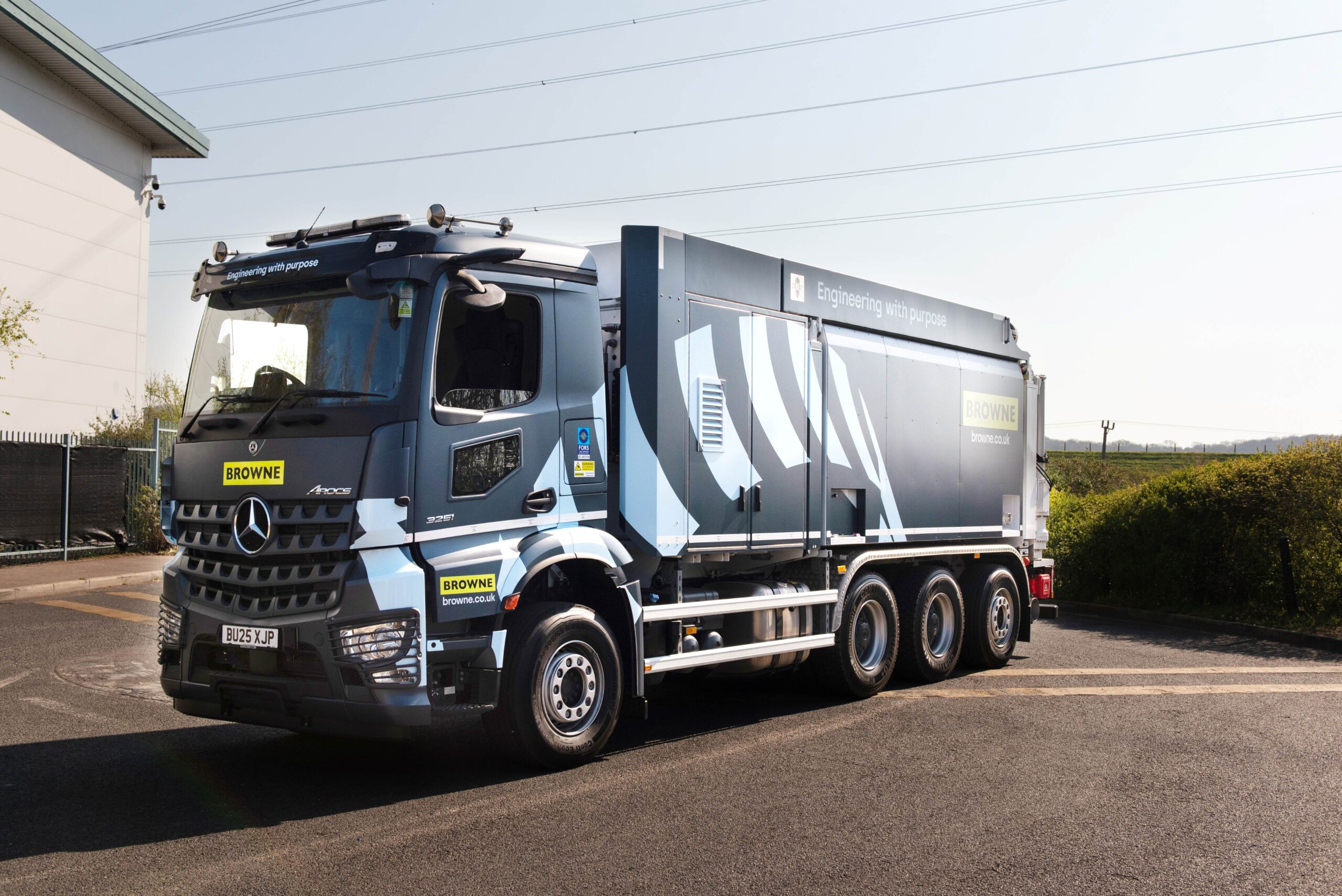 Enisca Browne - A large Browne branded Mercedes-Benz truck is parked on a paved road near a building and green bushes.