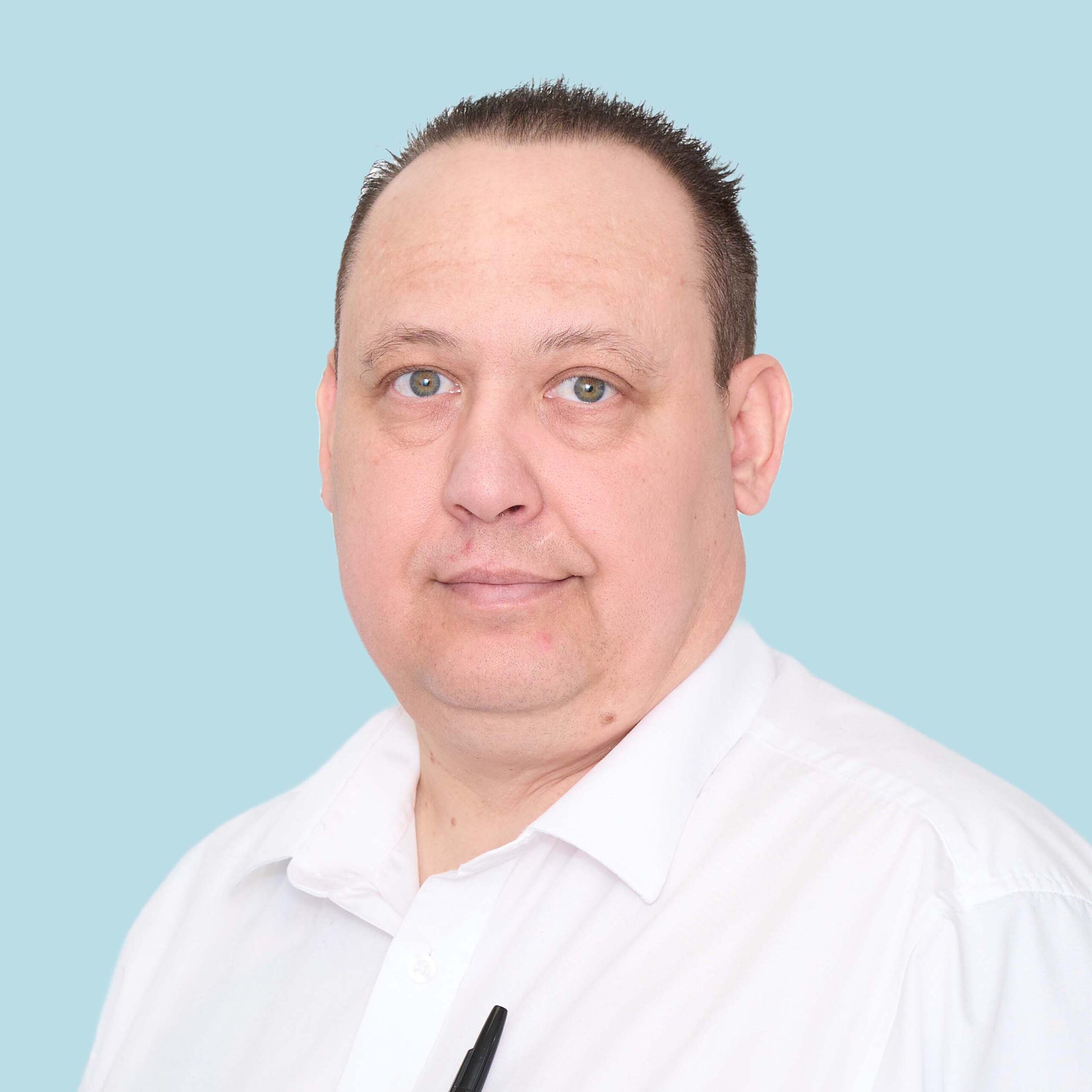 Enisca Browne - Man with short dark hair wearing a white shirt, facing forward against a light blue background.