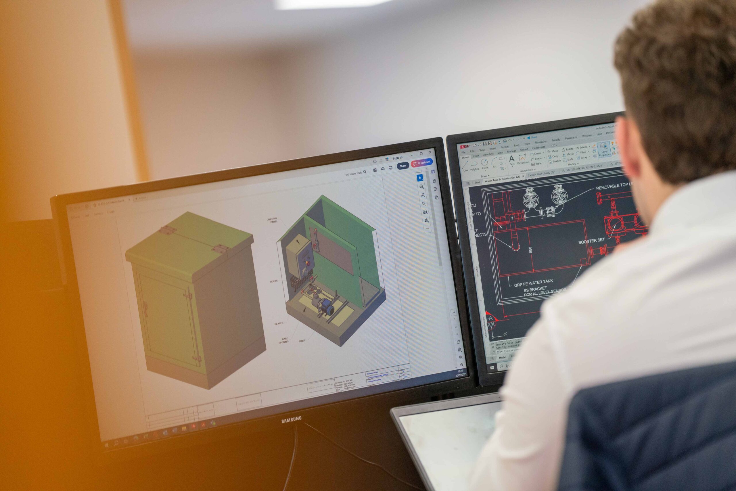 Enisca Browne - A person works at dual monitors displaying 3D modeling and technical drawings of a cabinet or enclosure.
