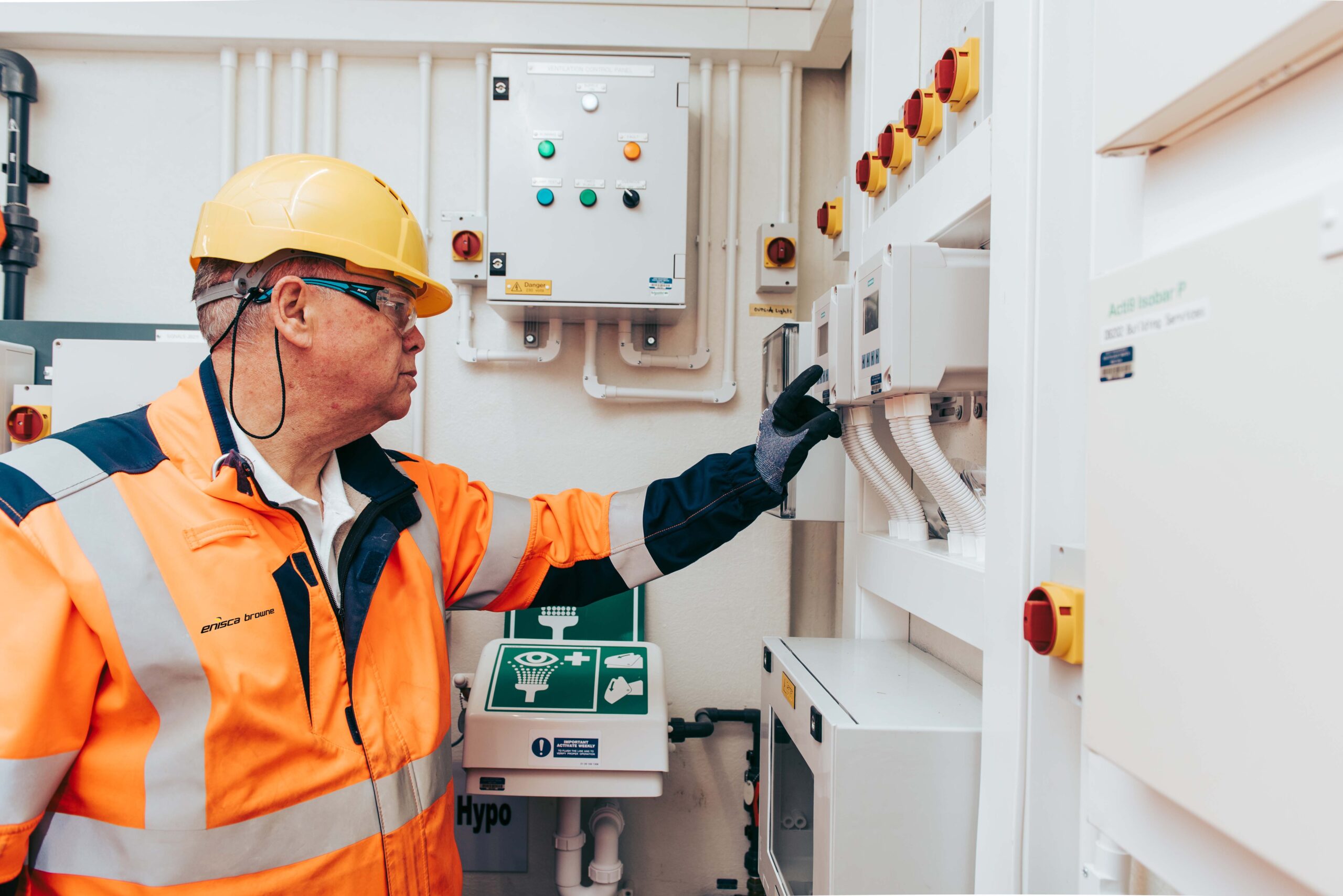 Enisca Browne - A worker in safety gear operates a control panel in an industrial setting.