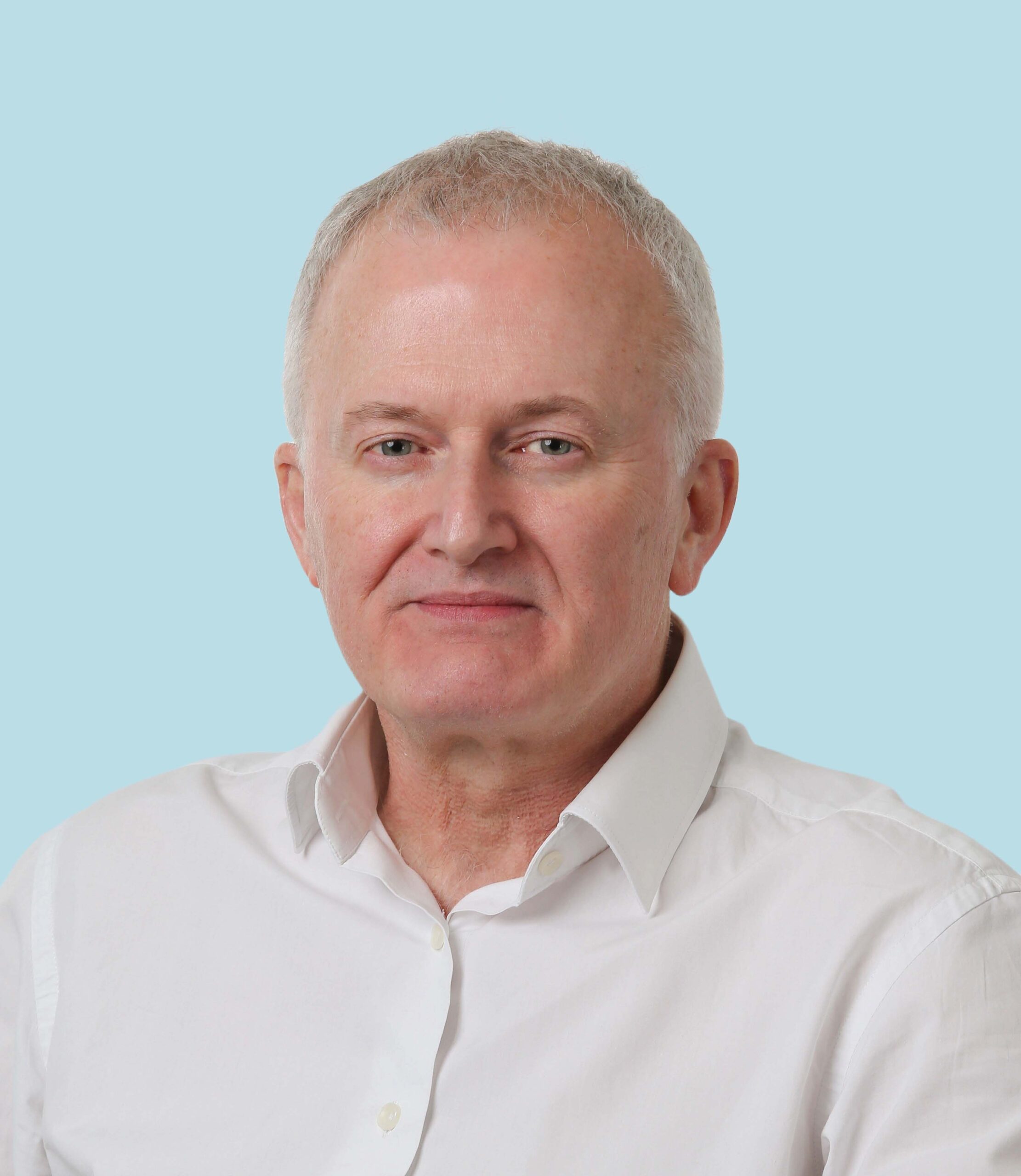 Enisca Browne - A middle-aged man with short gray hair wearing a white shirt, smiling slightly, on a light blue background.