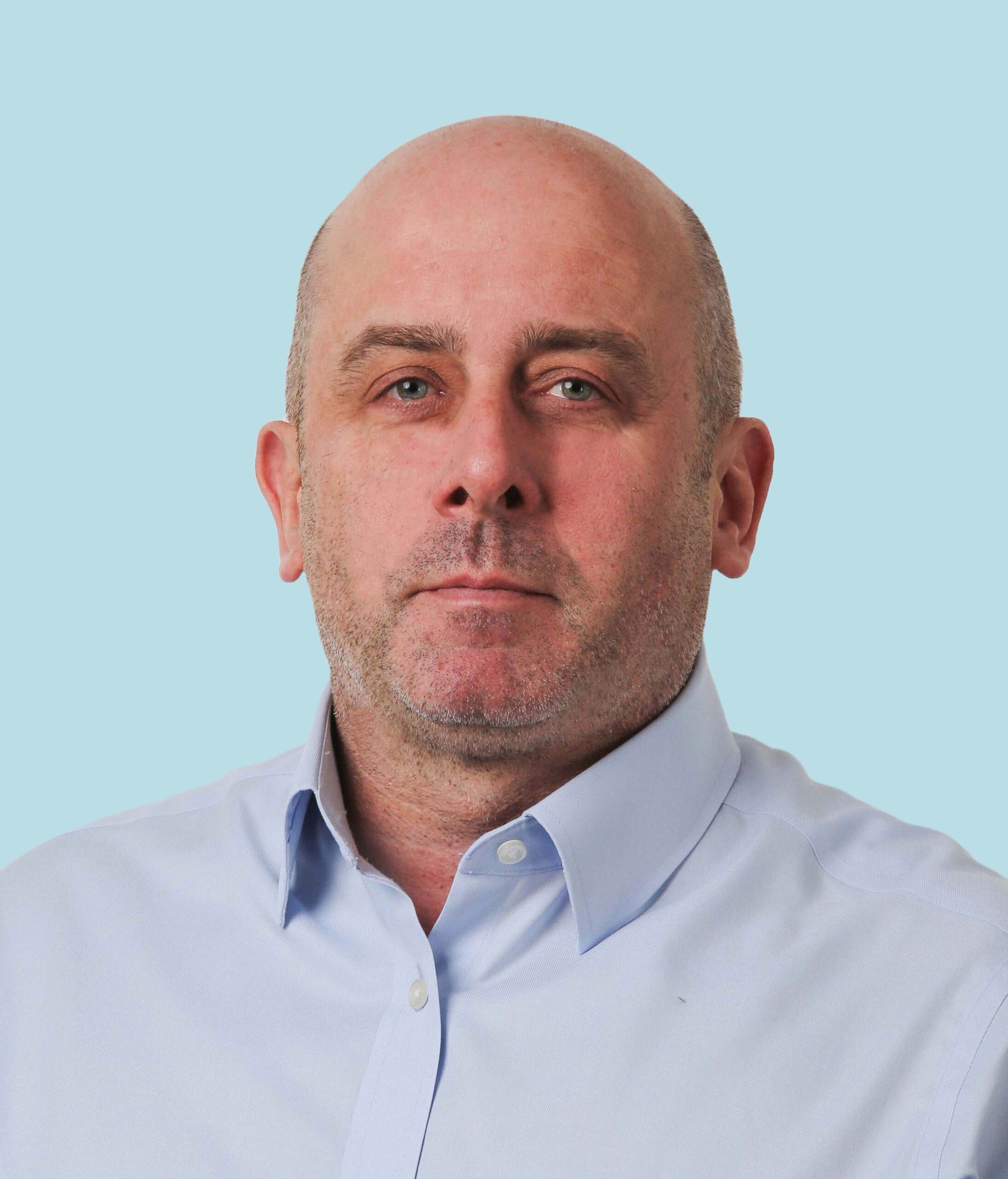 Enisca Browne - A bald man with a light beard wearing a light blue shirt against a light blue background.
