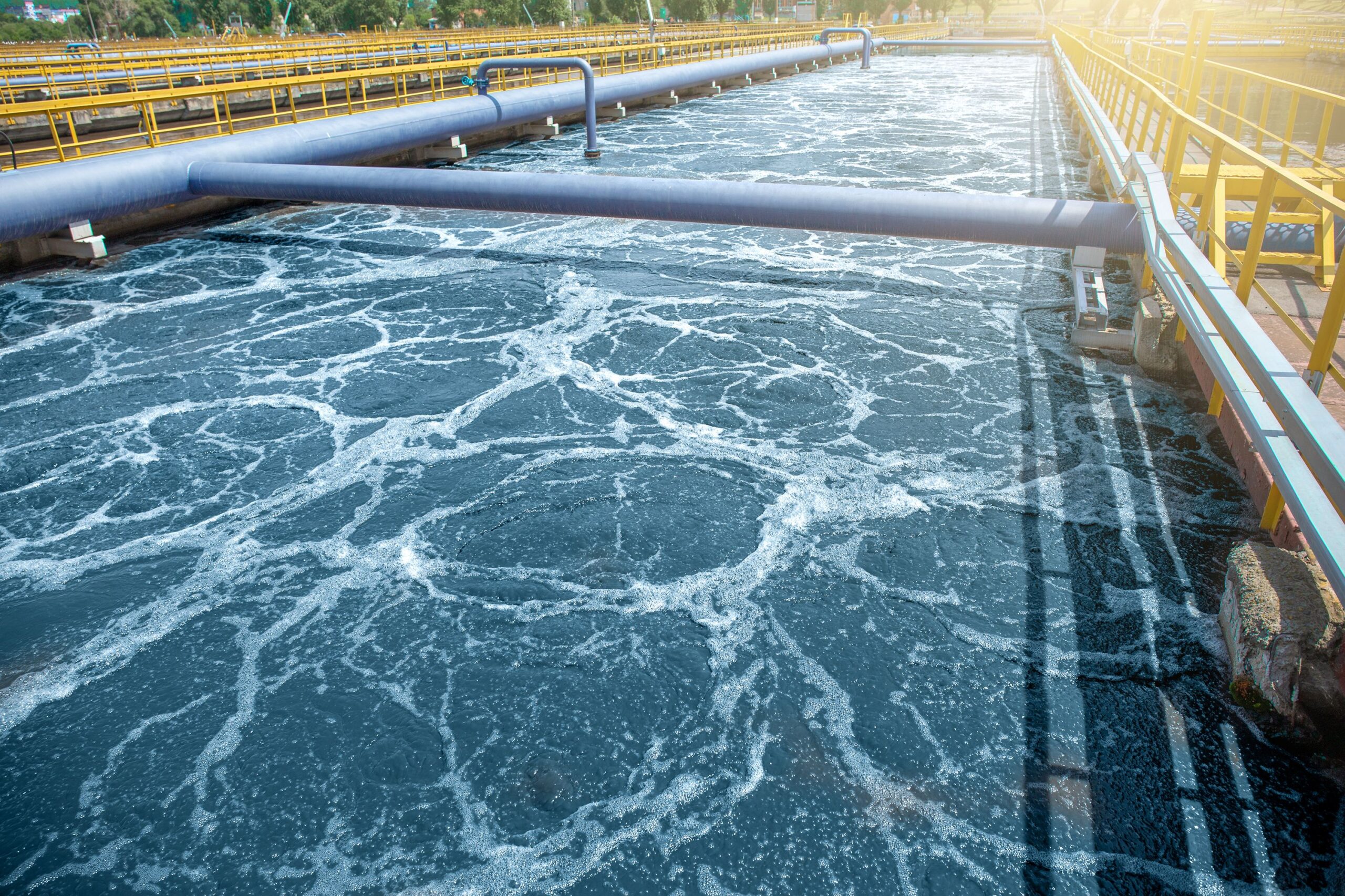 Enisca Browne - Aeration tank at a wastewater treatment plant with bubbles and pipes above churning water.